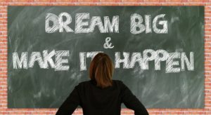 the chalk board illustrating dream big, and make it happen, with a student in front of it.