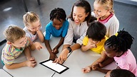 The picture of a teacher engaging with six of her students with a fun learning tablet.